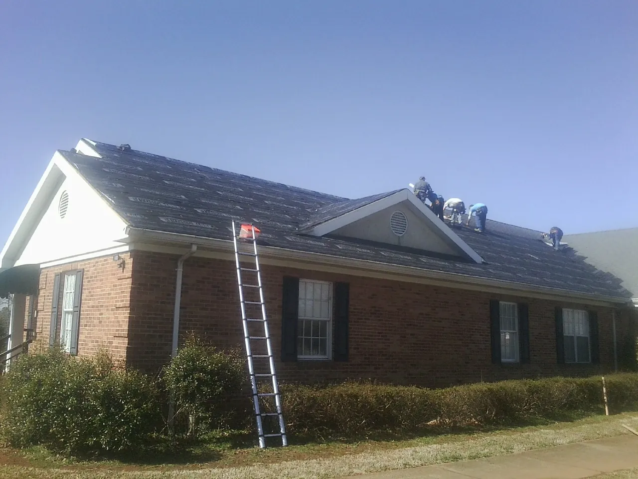 Crew tearing shingles off a brick ranch roof with a ladder set — Emergency Roof Repair work by our crew in Lacey